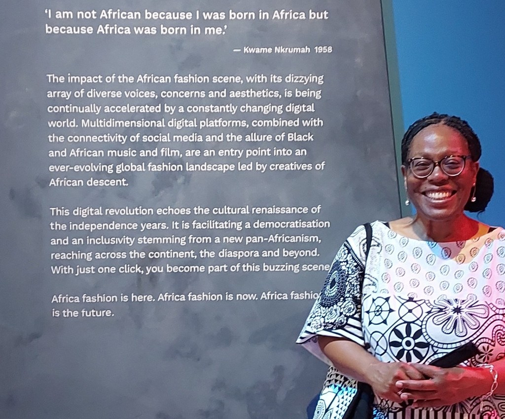 Carol Ann Dixon, Ph.D. photographed next to a display panel at the Africa Fashion exhibition, V&A Museum, London, August 2022.