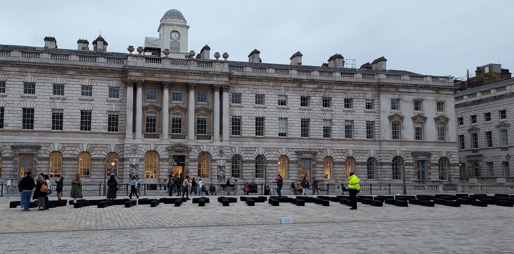 The west wing of the art gallery Somerset House (an 18th century building), with a contemporary art installation comprising 140 rectangular wooden blocks displayed in the courtyard in front of the building. The blocks are configured in the shape of a boat, representing a 32-metre-long, 18th century British slave ship.