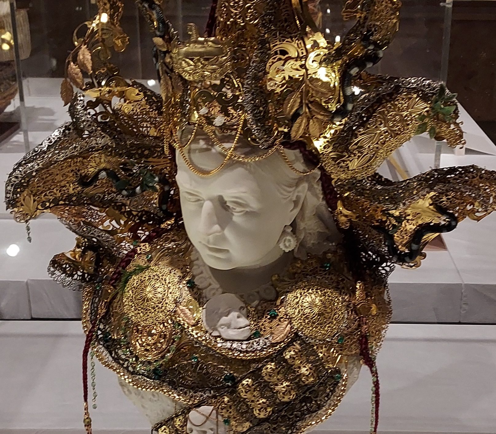 Art installation featuring a Parian ware bust of Queen Victoria embellished with costume jewellery and other decorative metalwork.