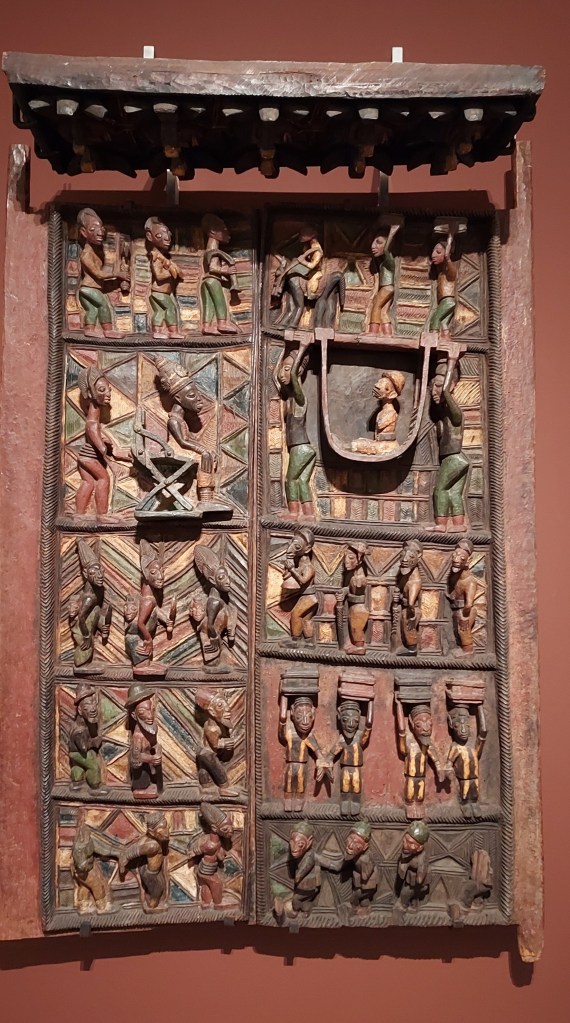 Pair of carved and painted wooden door panels with a lintel, created between c.1910 and 1914. The carving depicts a meeting between the king (Ogoga) and queen of Ikere meeting a British naval officer, Captain Ambrose, in c.1895, attended by courtiers and servants.